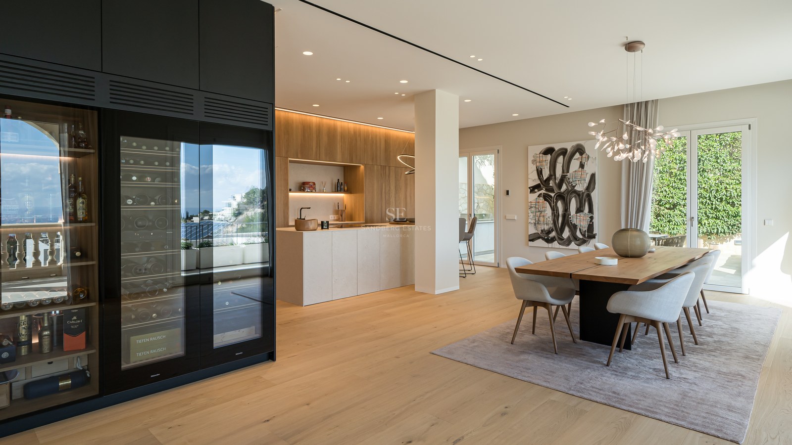 Comedor moderno de planta abierta con mesa de madera maciza, sillas tapizadas y vinoteca profesional empotrada.