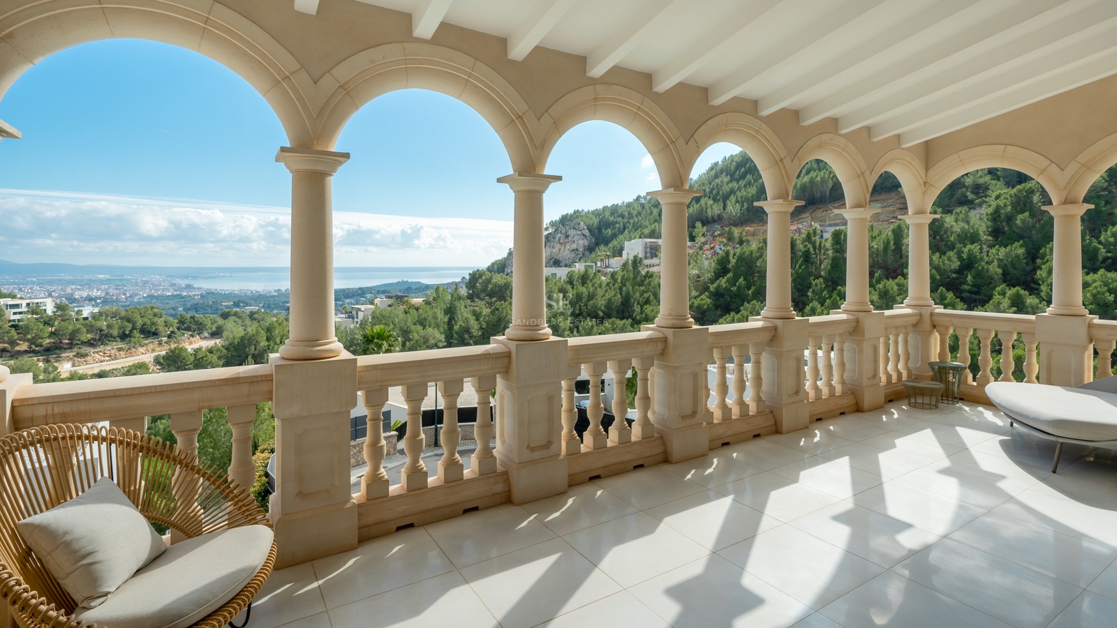 Terraza de piedra con arcos clásicos y vistas a colinas verdes, el mar y la silueta de la ciudad.