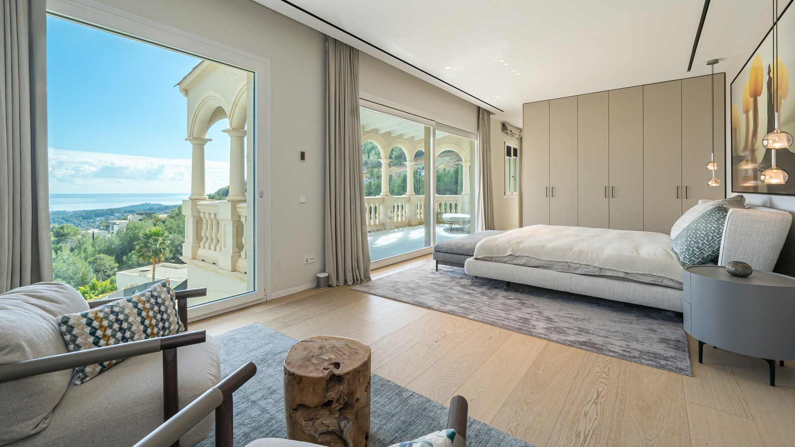 Dormitorio principal moderno con ventanales de suelo a techo, suelos de roble claro y balcón privado con vistas a la costa.