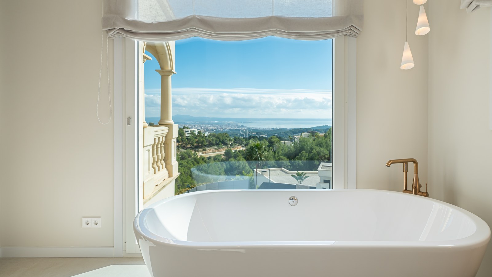 Bañera exenta blanca frente a un gran ventanal con vistas panorámicas a la costa y la ciudad.