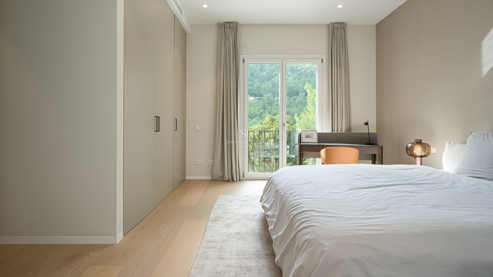 Dormitorio moderno con armarios de suelo a techo, suelos de madera clara y puertas francesas con vistas al bosque.