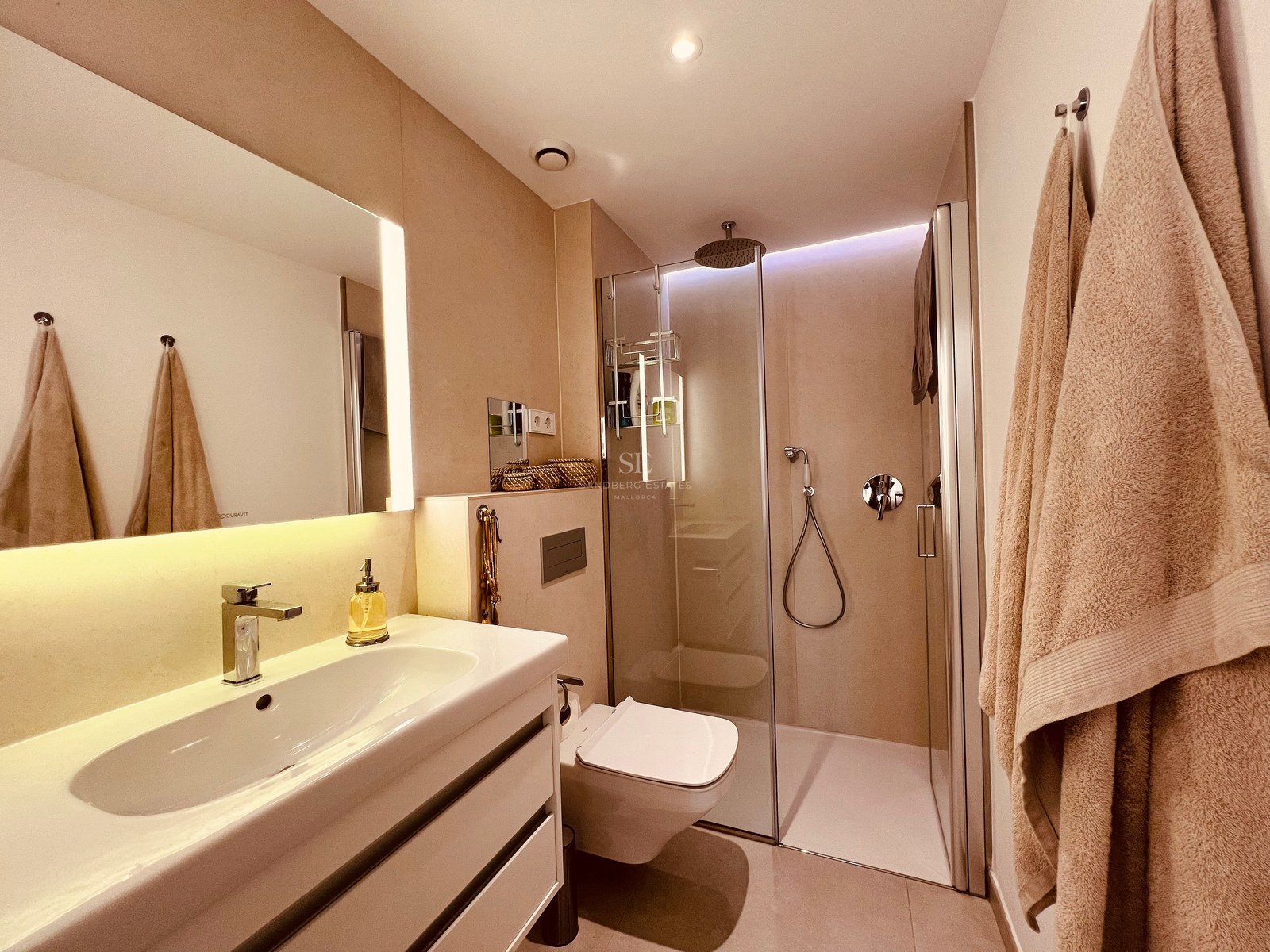 Modern bathroom featuring a walk-in glass shower, white floating vanity, and integrated warm LED lighting.