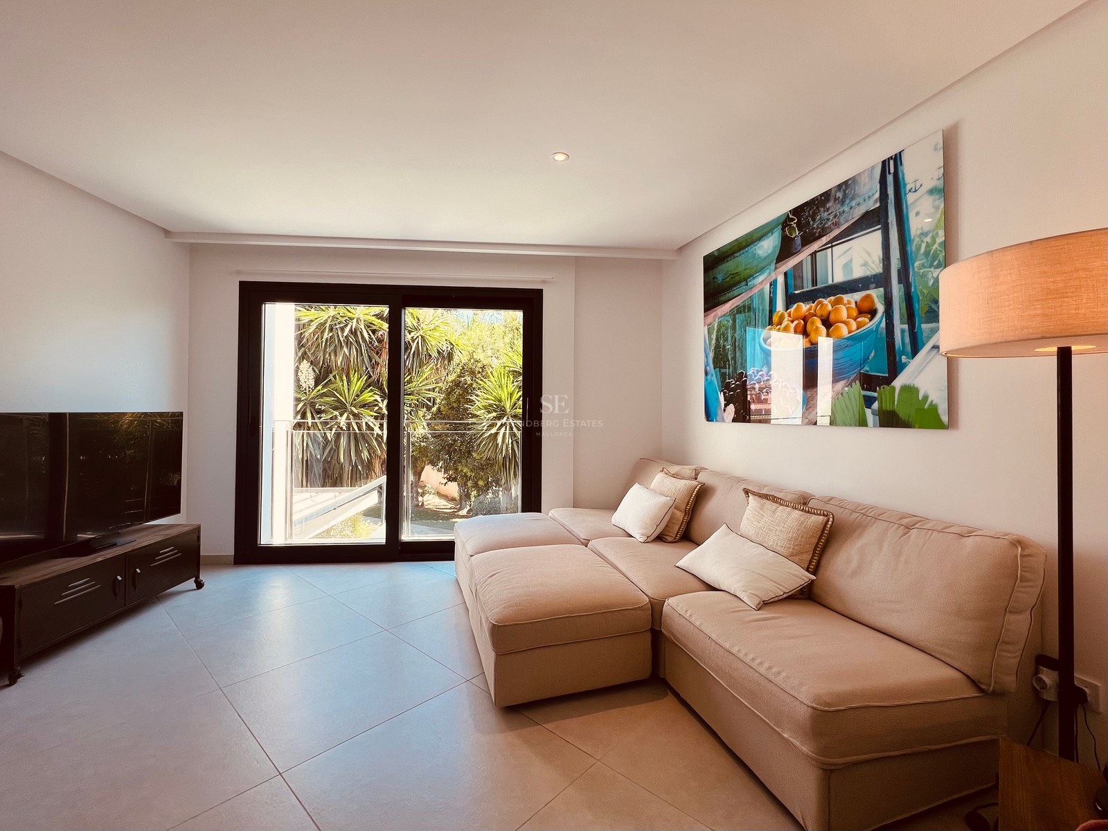 Modern living room featuring a beige sectional sofa, large wall art, and sliding doors opening to a lush terrace.