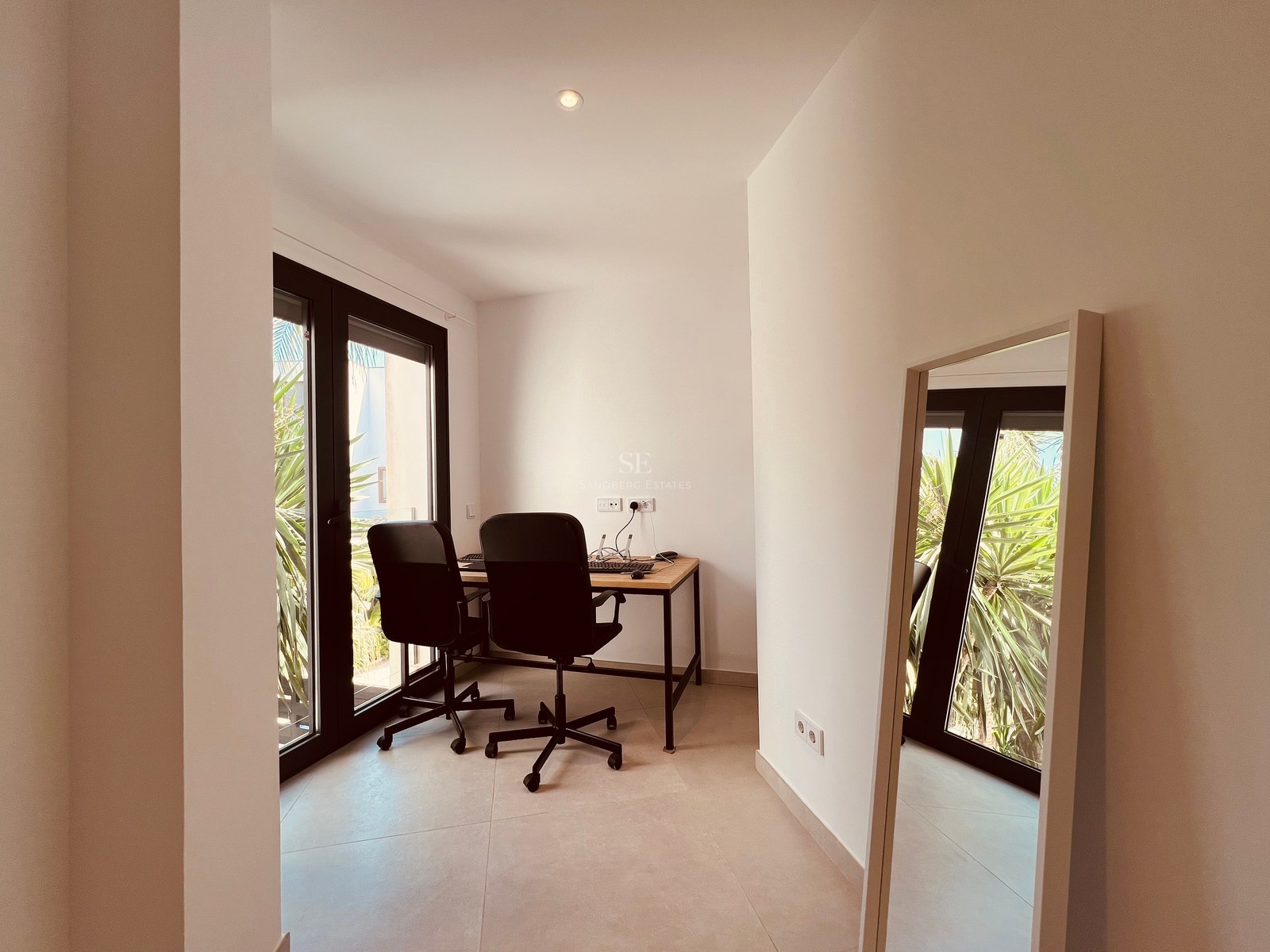 Bright contemporary home office featuring a wooden desk, two ergonomic chairs, and large glass doors to the garden.