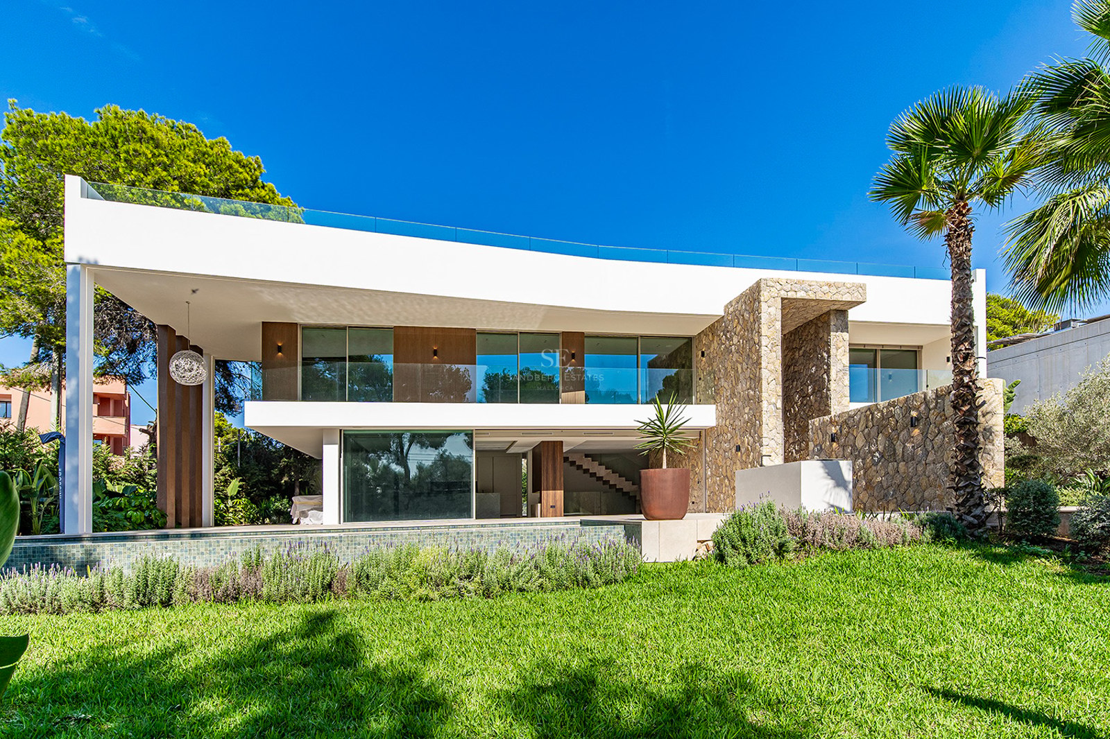 Exterior of a white two-story modern villa with stone walls, glass balconies, pool, and manicured green lawn.