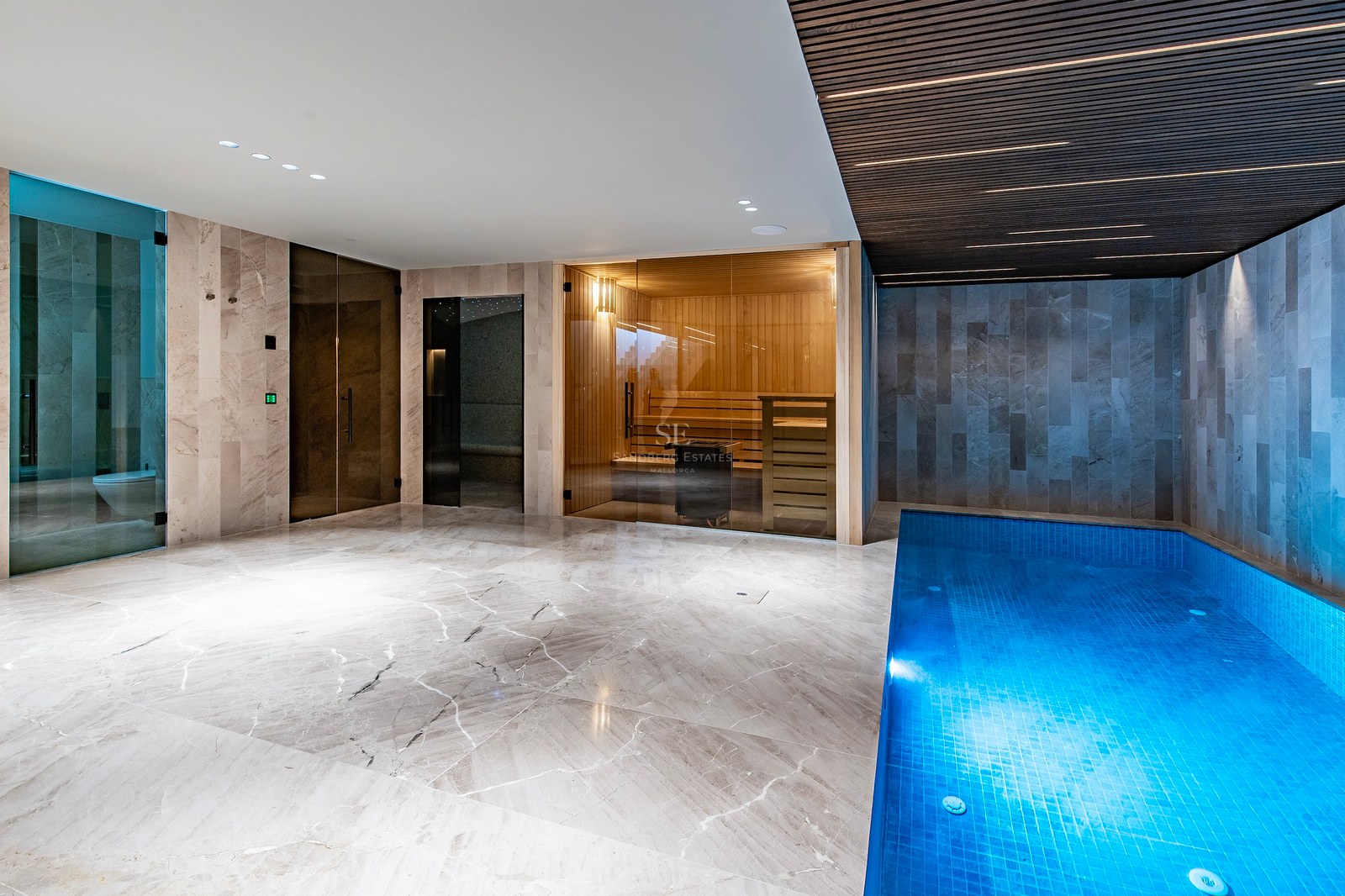 Indoor spa with a small blue pool, glass-walled sauna, and marble floors under a slatted ceiling.