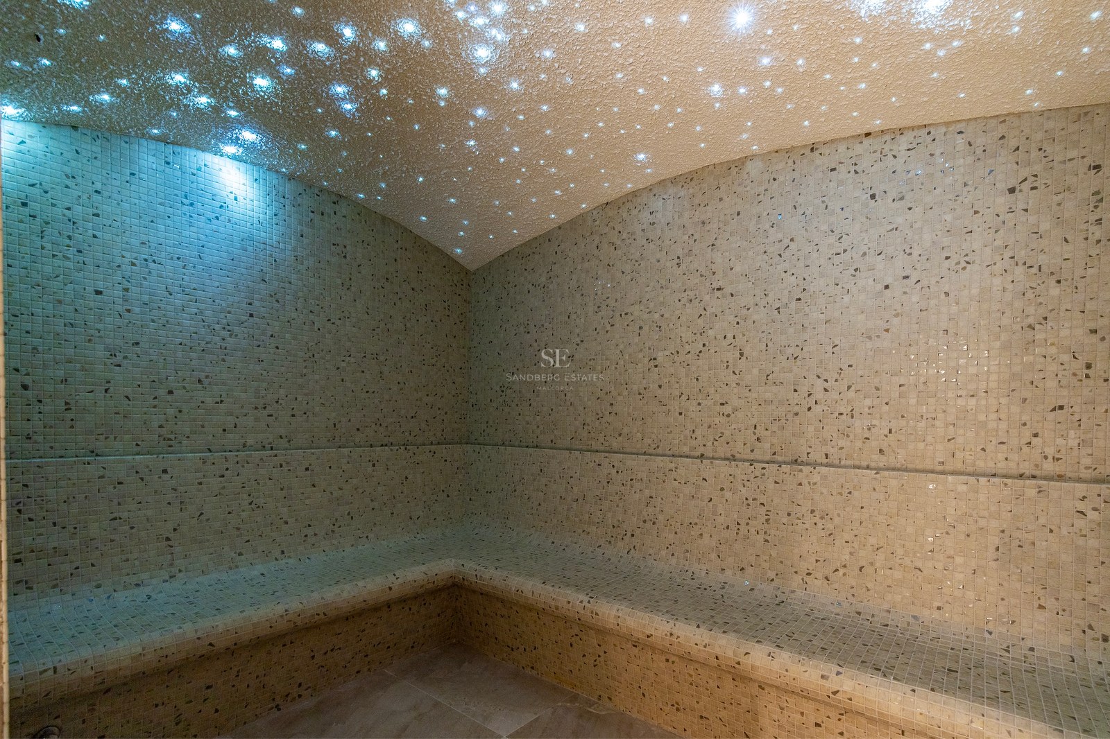 Luxury steam room featuring beige mosaic tiles and a fiber-optic starry sky ceiling lighting effect.