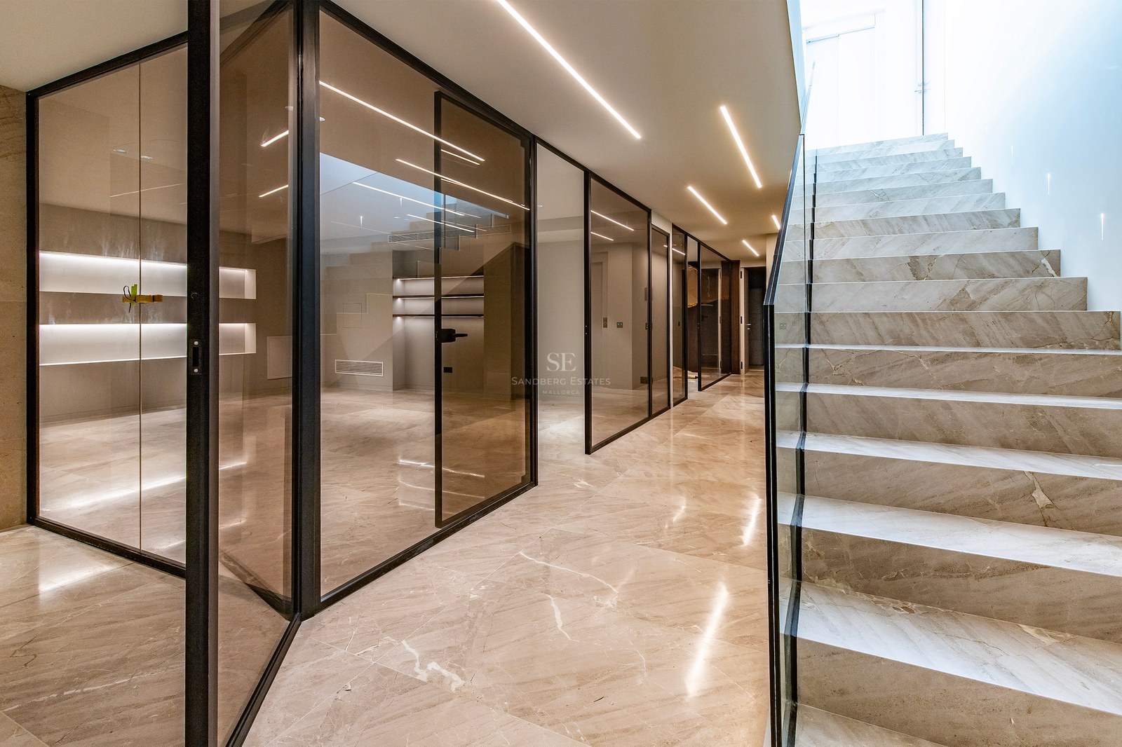 Modern interior hallway featuring a marble staircase, floor-to-ceiling glass partitions, and linear LED ceiling lighting.