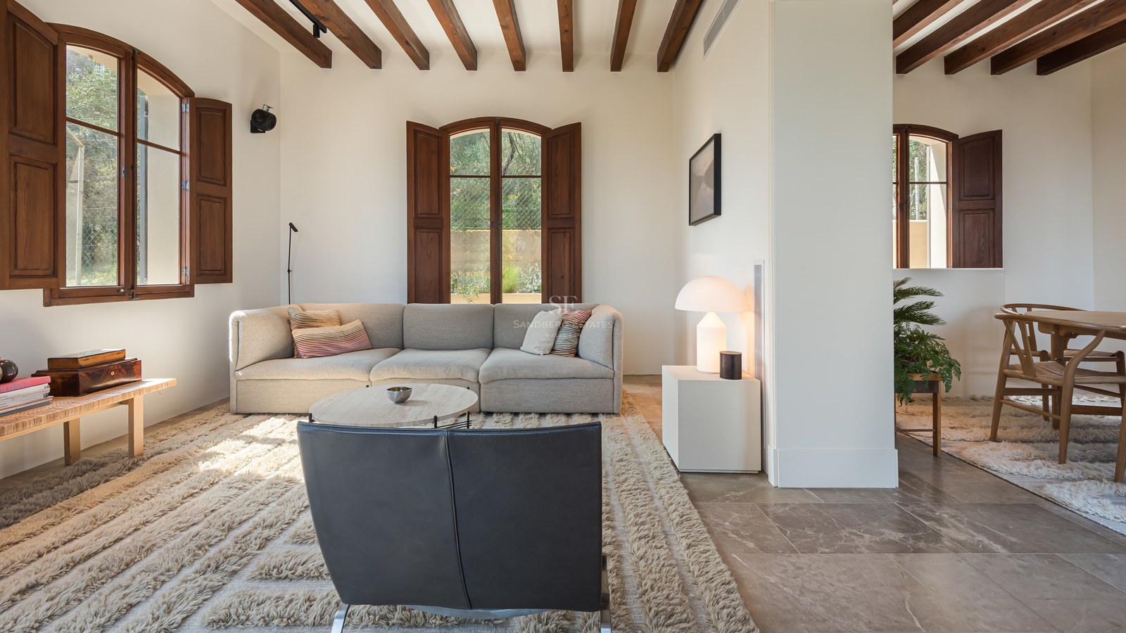 Salon contemporain avec poutres en bois foncé, sol en pierre naturelle et mobilier design aux tons neutres.