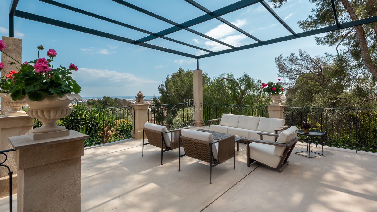 Terrasse ensoleillée avec mobilier lounge moderne, garde-corps en fer forgé et pergola métallique surplombant la côte.