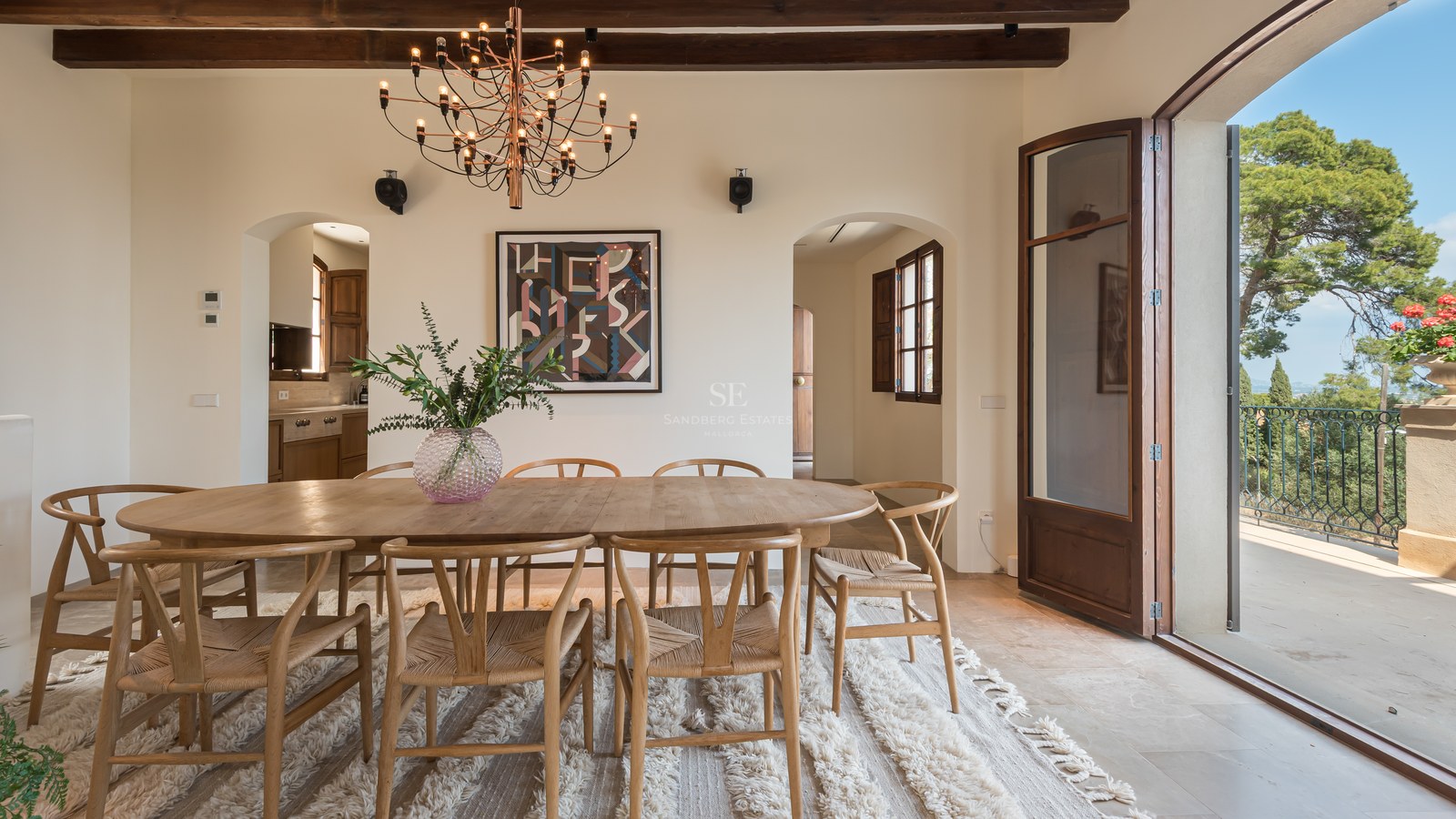 Table à manger ovale en chêne, chaises wishbone et poutres apparentes dans une luxueuse résidence méditerranéenne.