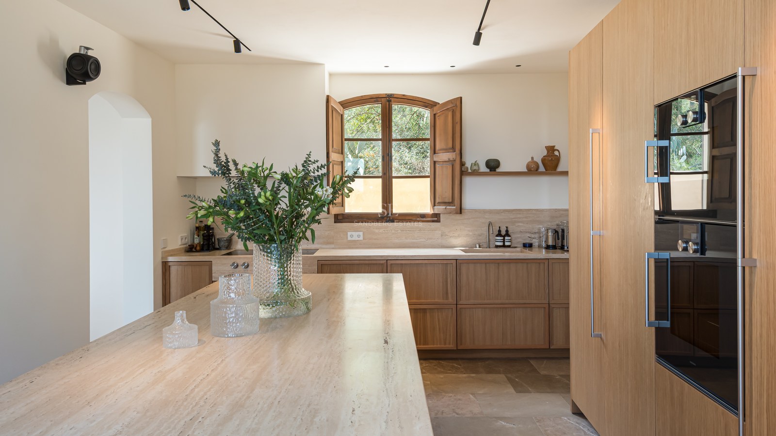Cuisine minimaliste avec placards en chêne clair, îlot en travertin et volets en bois traditionnels.