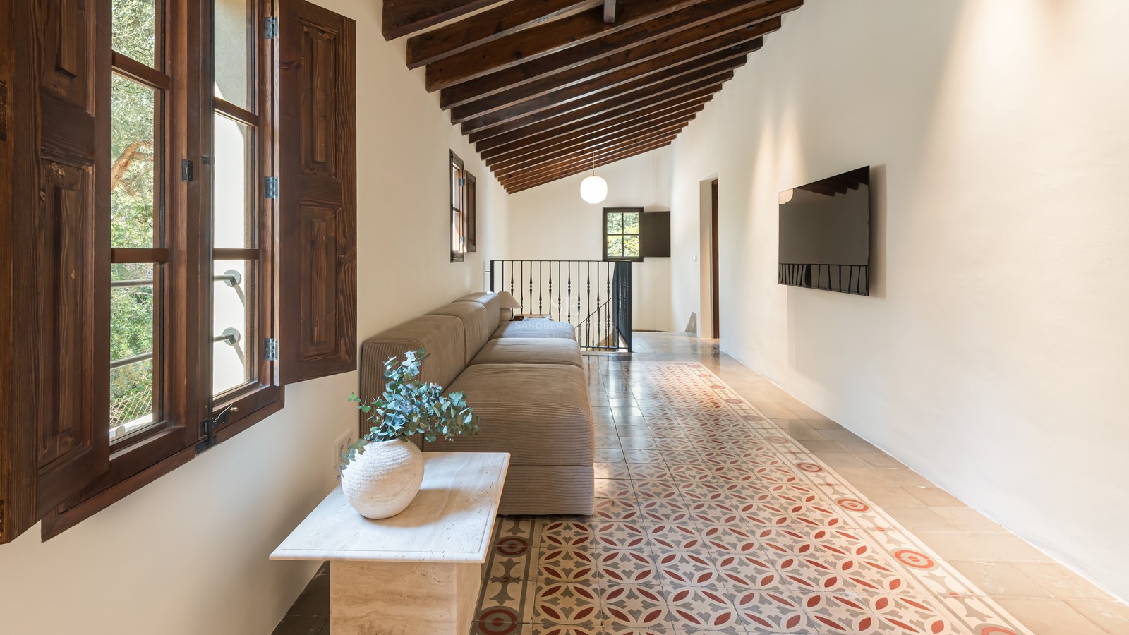 Espace de vie avec poutres apparentes, carreaux de ciment traditionnels, canapé modulaire et volets en bois.