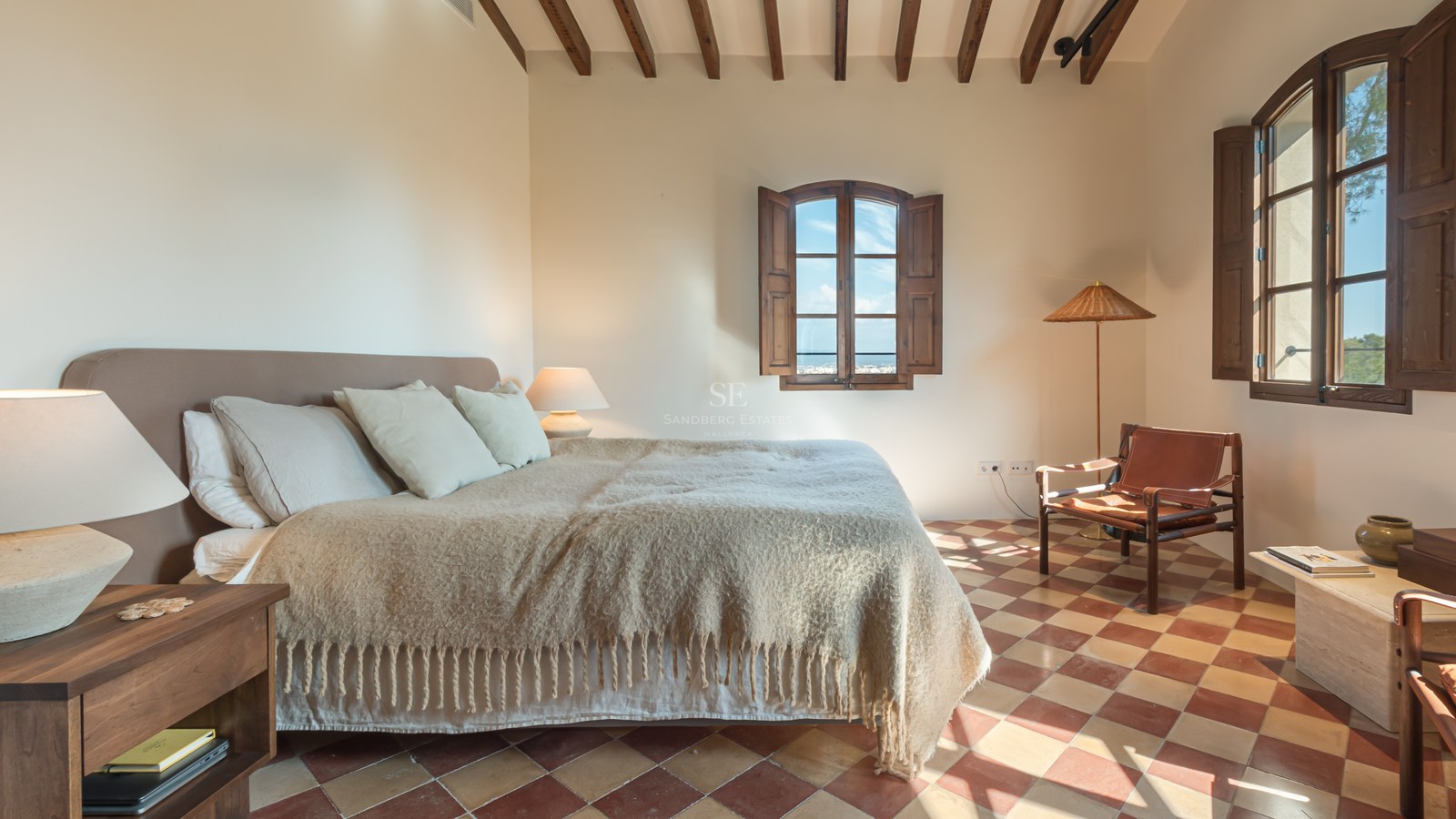 Chambre rustique avec sol en terre cuite, poutres apparentes et fenêtres à volets en bois donnant sur la côte.