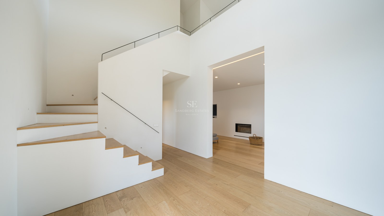 Modern minimalistisk hall med vita väggar, ljust ekparkettgolv och stilren vit trappa med svart räcke.