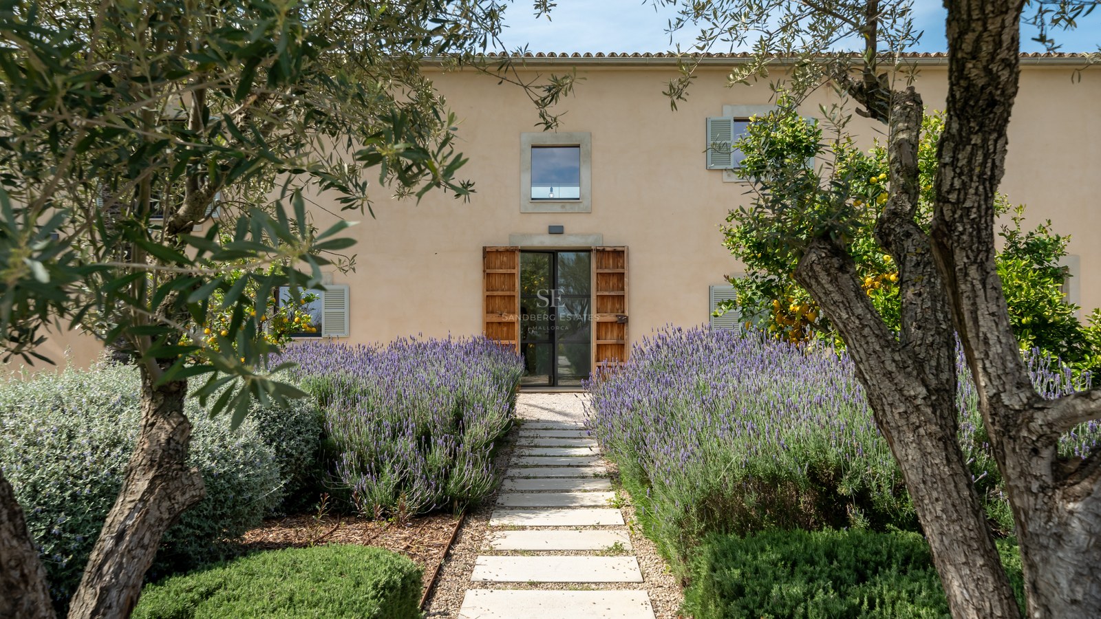 Stenstig omgiven av blommande lavendel leder till en modern glasdörr i en traditionell ockrafärgad villa.
