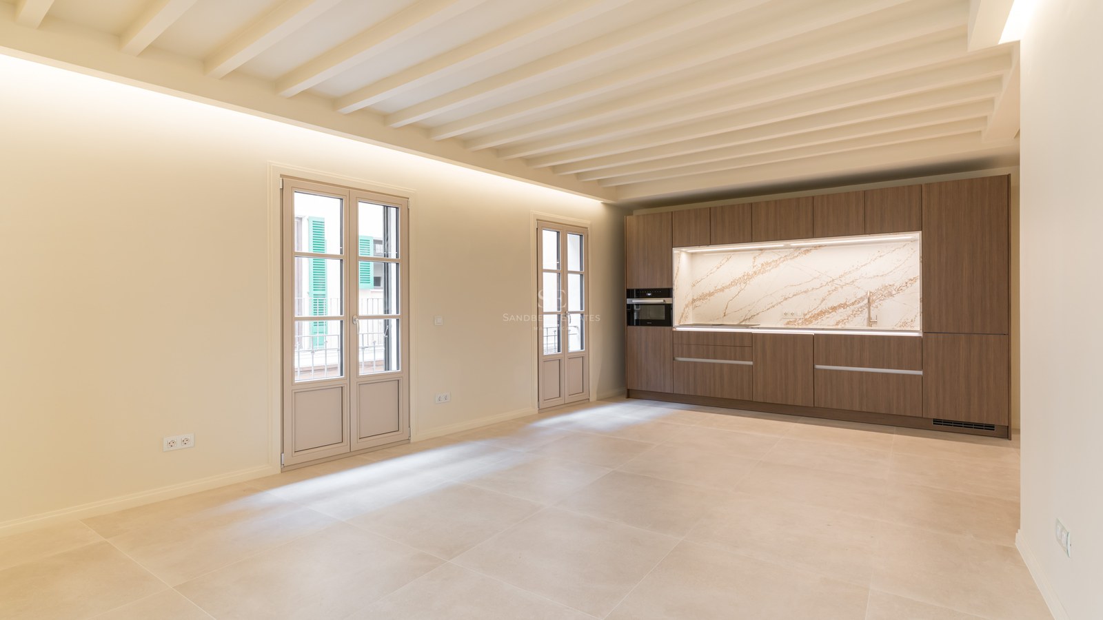 Cocina moderna con muebles de madera, encimera de mármol veteado, techos de vigas blancas y suelo de gres porcelánico.