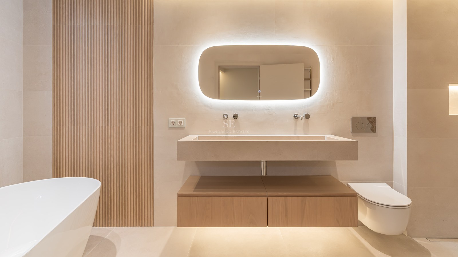 Baño contemporáneo con lavabo flotante de piedra, espejo retroiluminado, paneles de madera y bañera exenta.