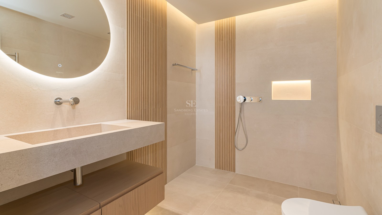 Baño moderno con espejo circular retroiluminado, lavabo de piedra integrada y paneles de madera verticales.