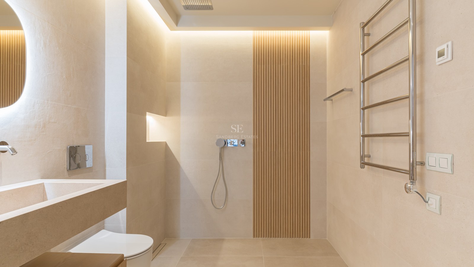 Baño moderno con azulejos beige, pared de listones de madera, ducha italiana y toallero de cromo.
