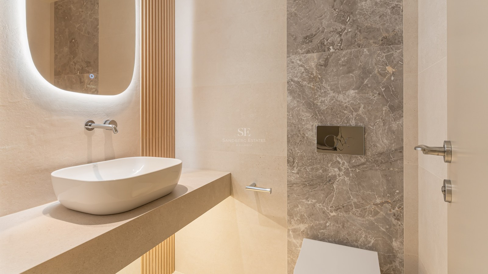 Aseo moderno con lavabo sobre encimera, espejo retroiluminado, listones de madera y pared de mármol gris.
