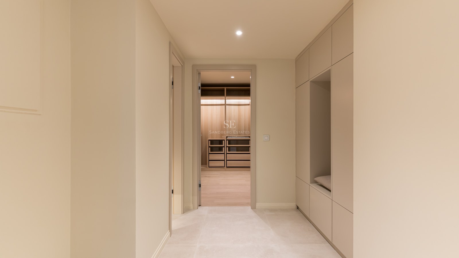 Pasillo con armarios minimalistas beige y banco integrado que conduce a un vestidor de madera iluminado.