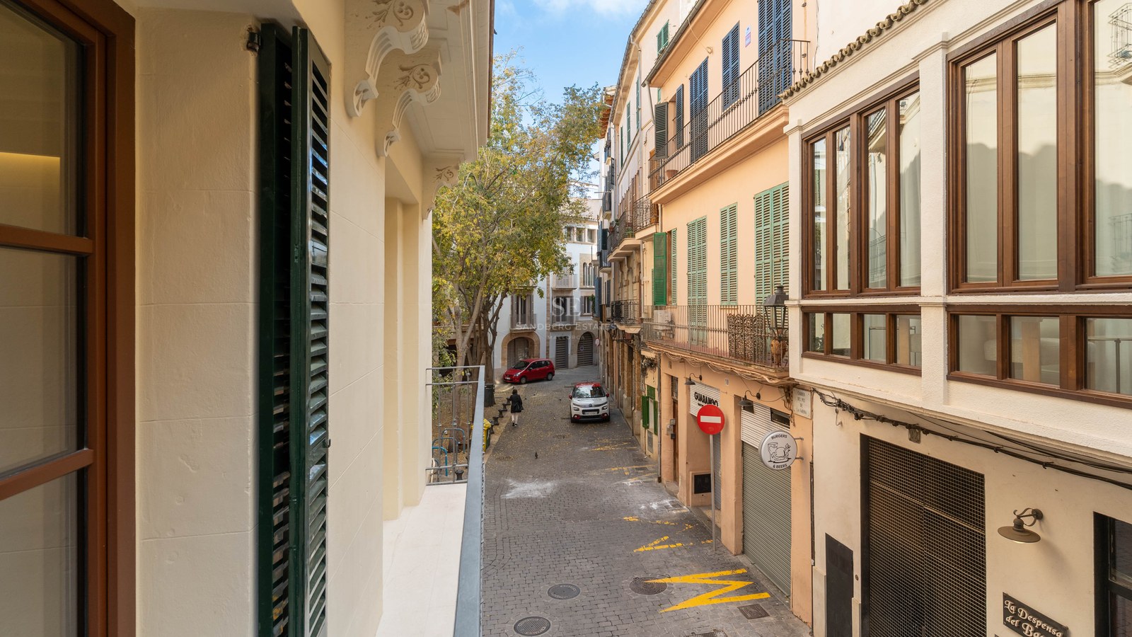 Calle estrecha empedrada con fachadas históricas y persianas mallorquinas tradicionales bajo un cielo despejado.