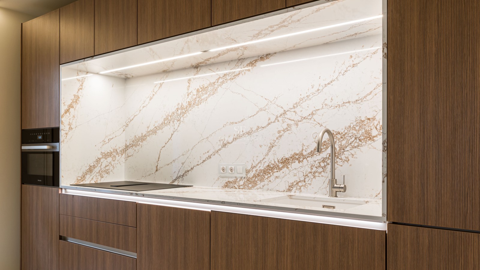 Cocina moderna con armarios de madera oscura, salpicadero de mármol con vetas marrones e iluminación LED integrada.