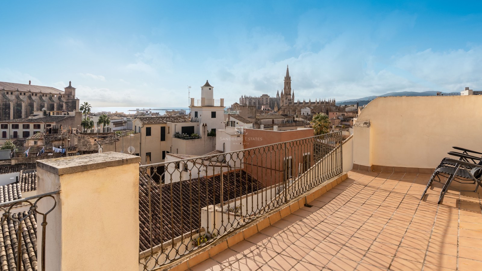 Terraza soleada con suelos de terracota y barandilla de forja con vistas a Palma de Mallorca y su catedral.