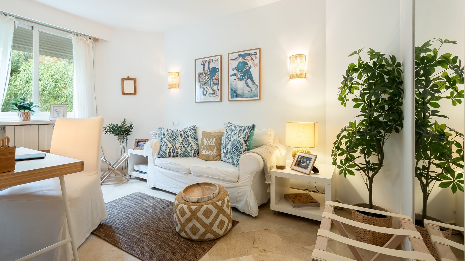 Bright living room featuring a white sofa, blue octopus wall art, marble flooring, and a large window overlooking greenery.