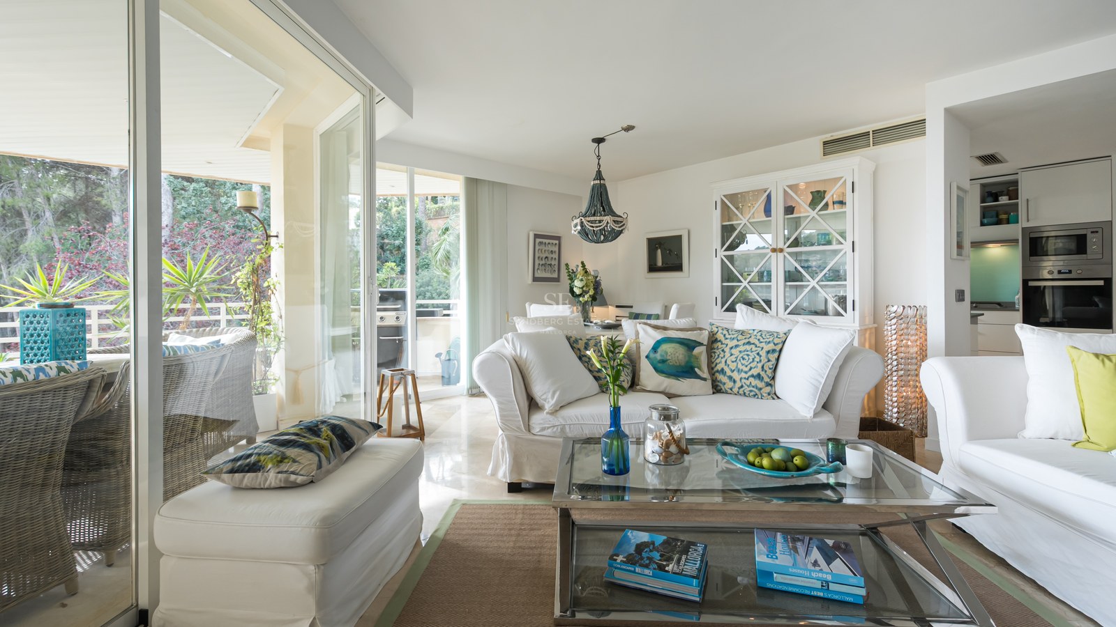 Open-plan living room featuring white sofas, a glass coffee table, and large sliding glass doors leading to a terrace.