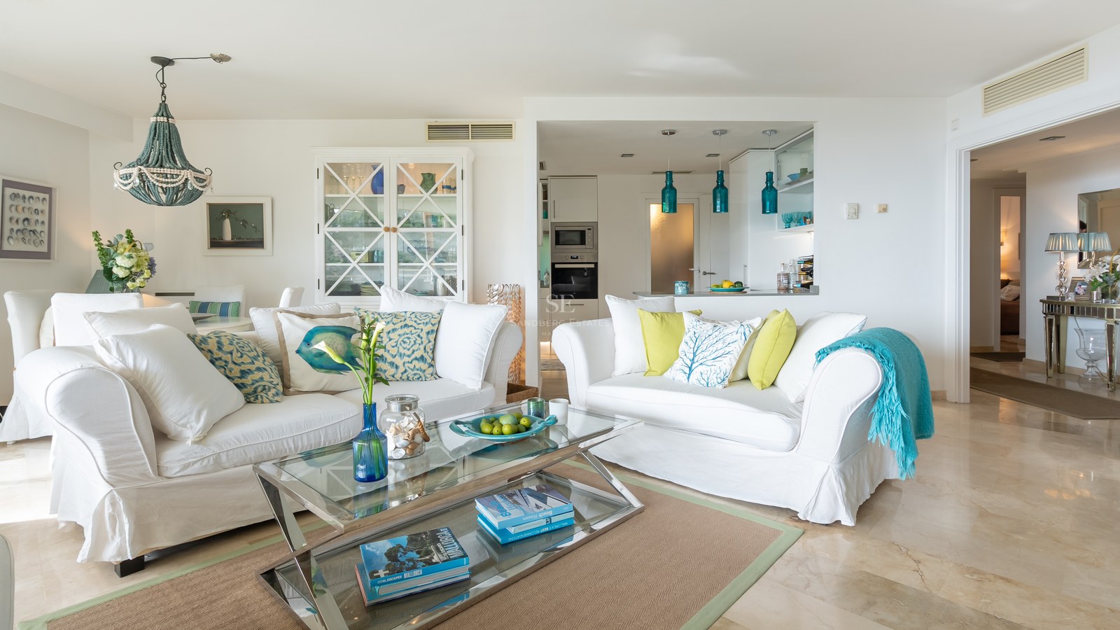 Bright living room with two white sofas, a glass coffee table, marble floors, and Mediterranean decor elements.