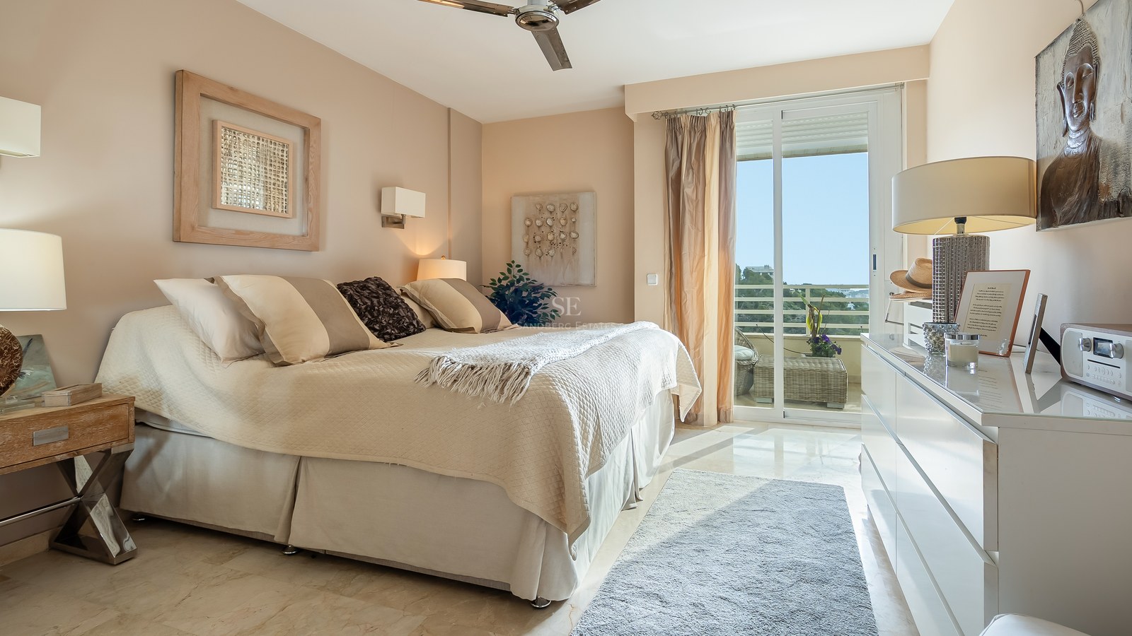 Bright bedroom with cream bedding, marble floors, and sliding glass doors opening to a sunlit terrace.