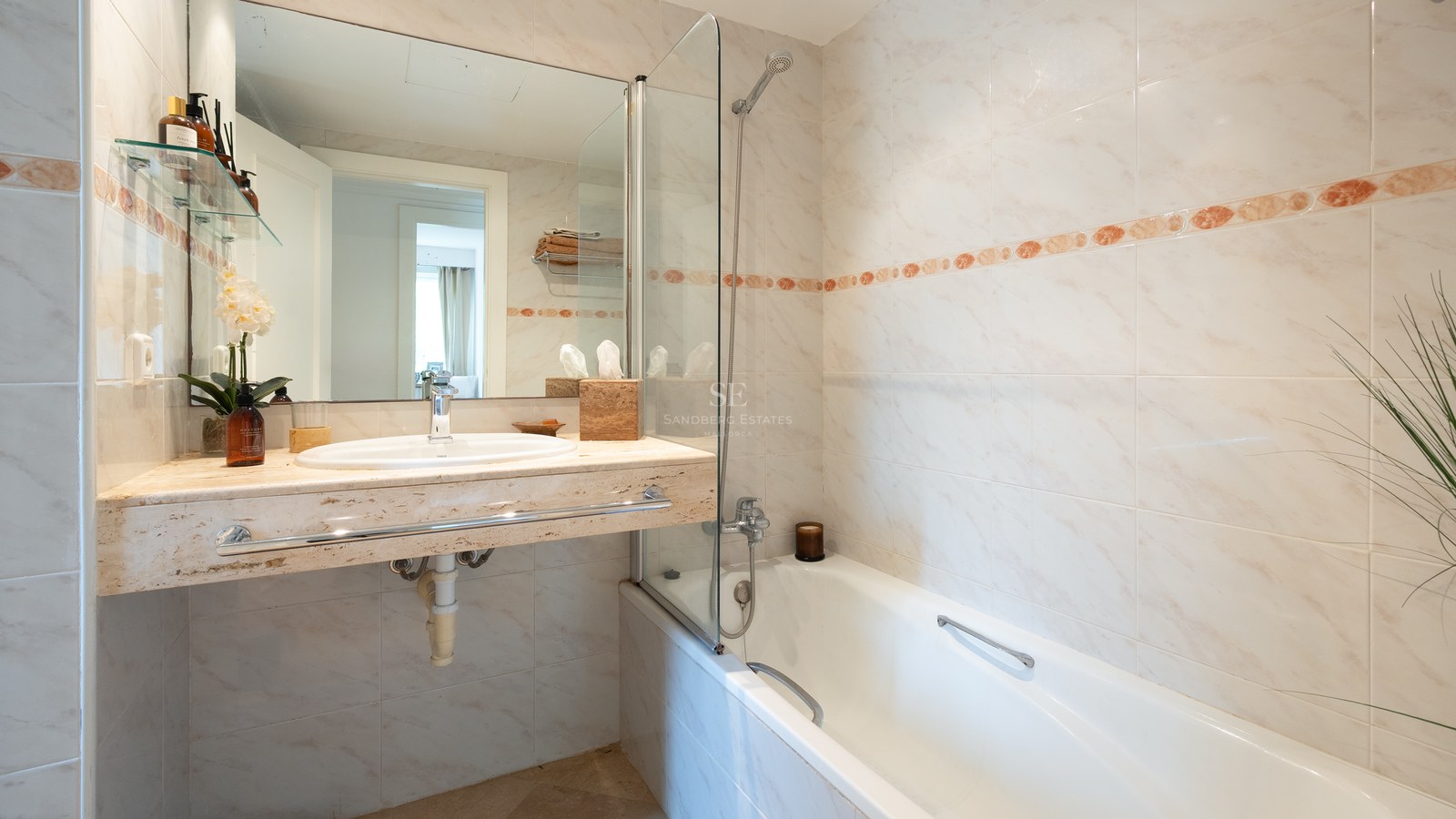 Bathroom featuring a bathtub with glass screen and a cream-colored marble vanity with an inset sink.