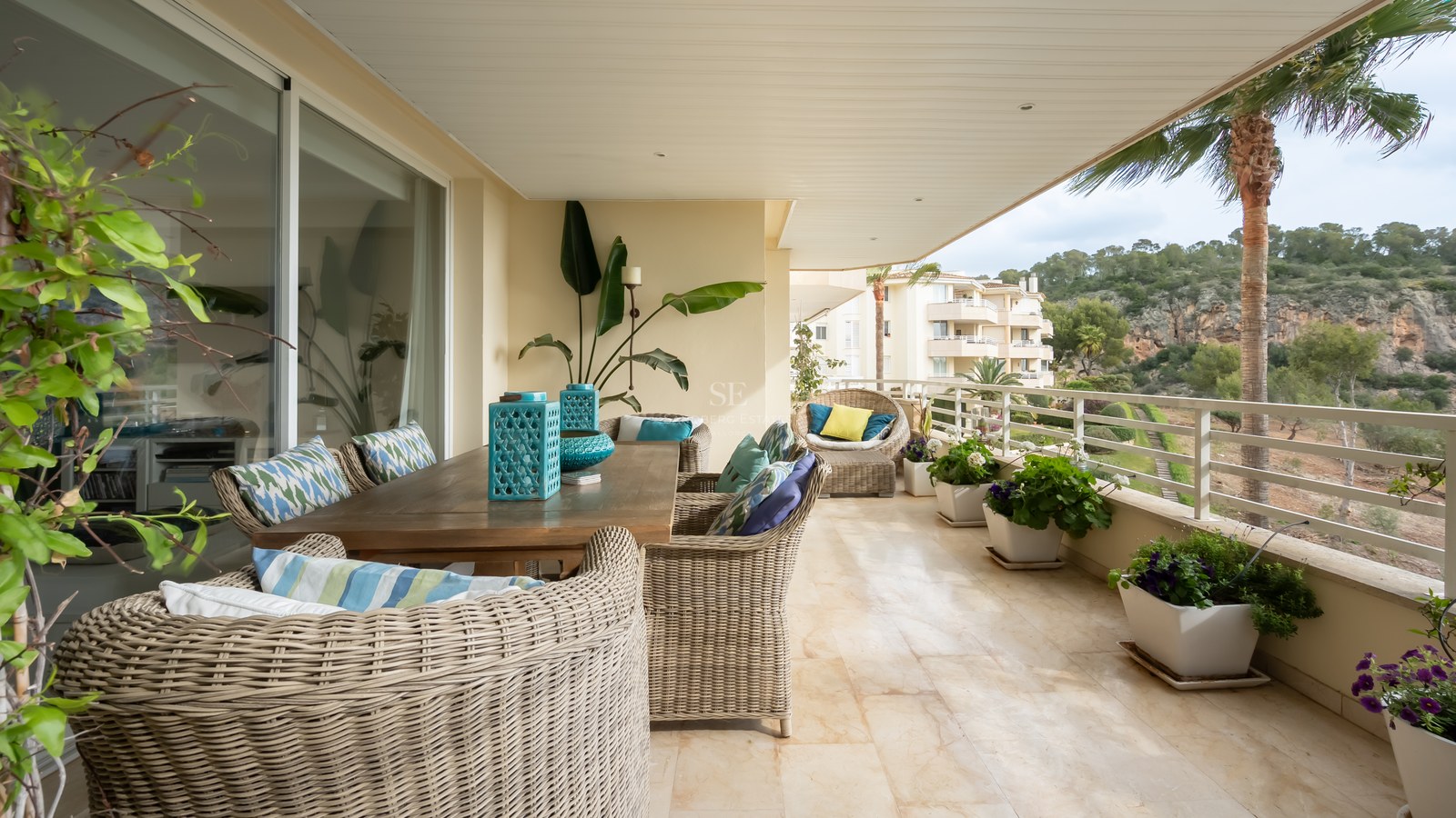 Spacious covered terrace with marble floors, wicker dining furniture, and views of lush hills and palm trees.