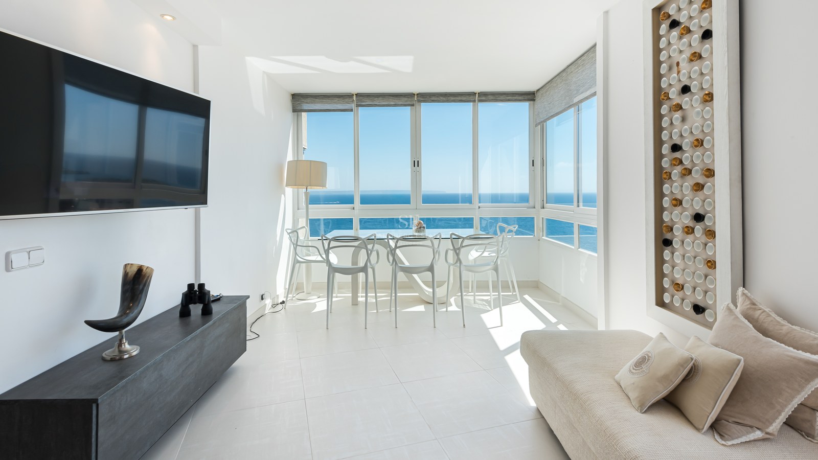Bright modern living room featuring full-length windows with panoramic views of the Mediterranean sea and white furniture.