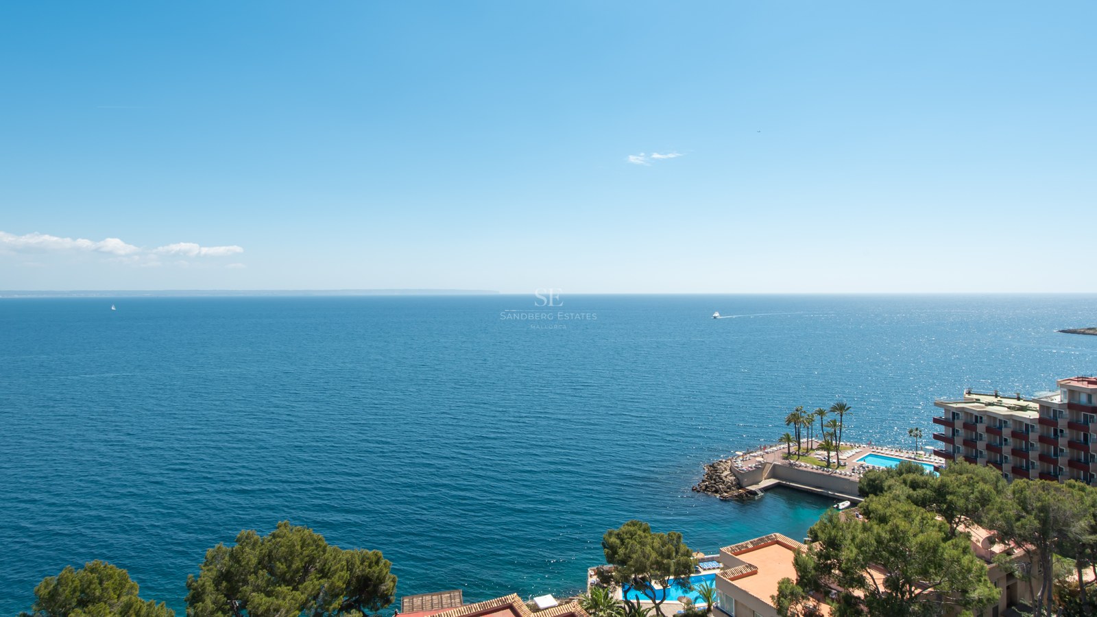 High-angle view of the blue Mediterranean sea with coastline buildings and swimming pools under a clear sky.
