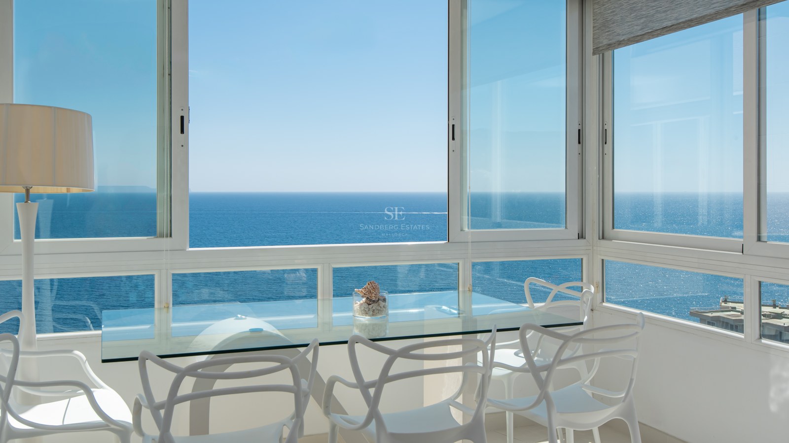 Modern dining area with white designer chairs and glass table overlooking the calm blue Mediterranean sea.