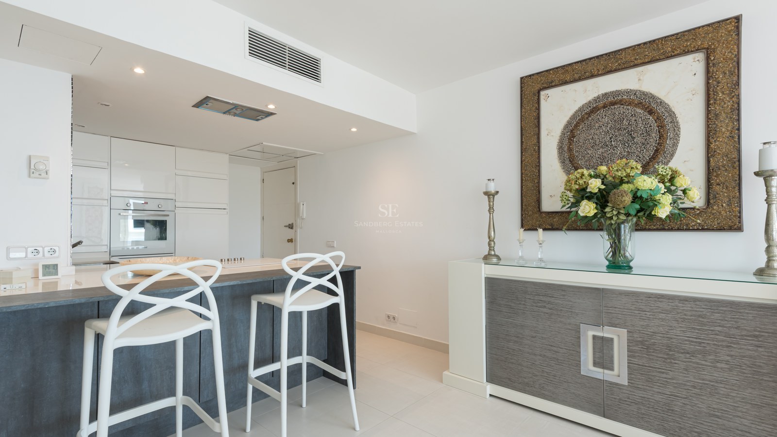 Modern white kitchen featuring a charcoal grey island, white designer bar stools, and a stylish sideboard.