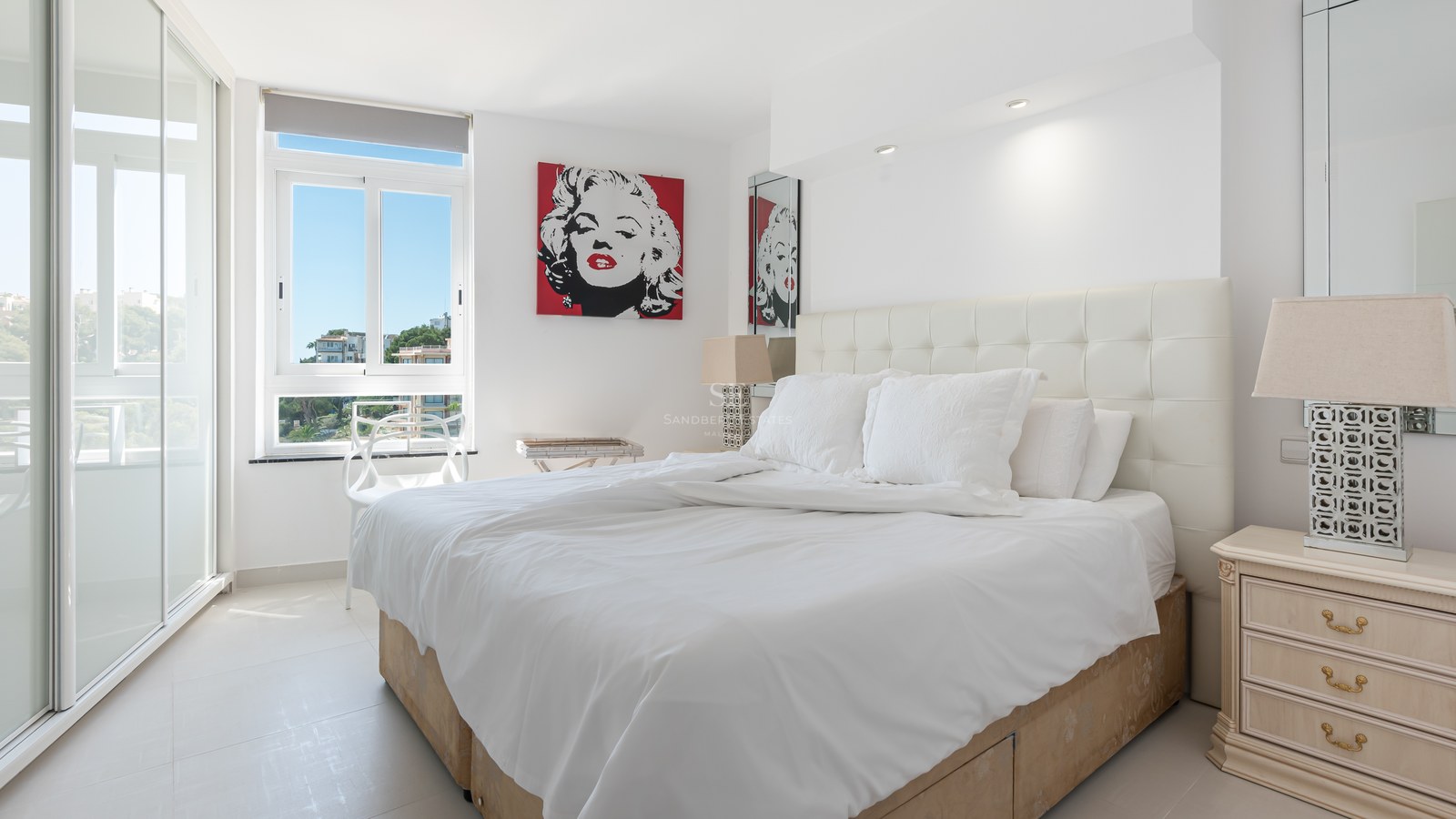 Modern bedroom featuring a white tufted headboard, large sliding glass doors, and vibrant pop art.