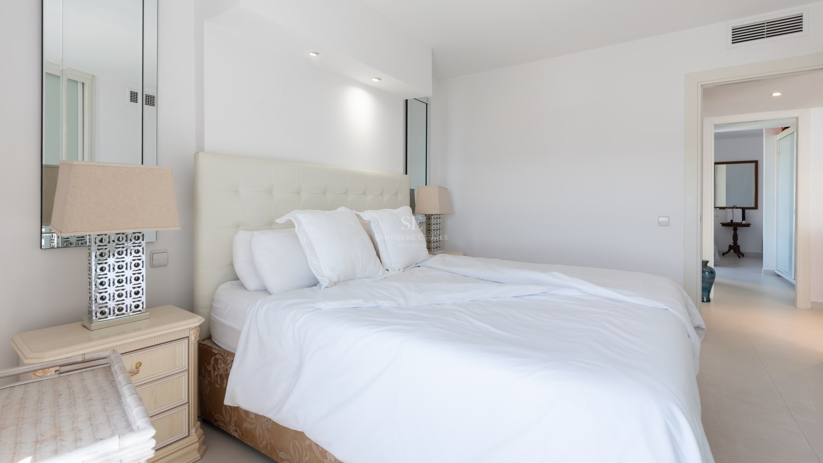 Bright bedroom featuring a white tufted headboard, symmetric bedside tables with lamps, and clean tiled floors.