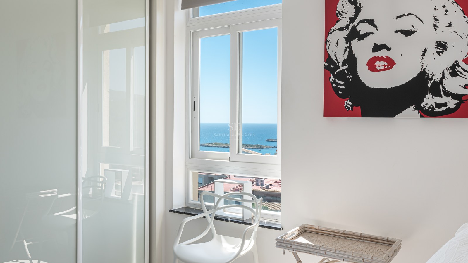 Bright white bedroom with a window overlooking the Mediterranean sea and sleek fitted wardrobes.
