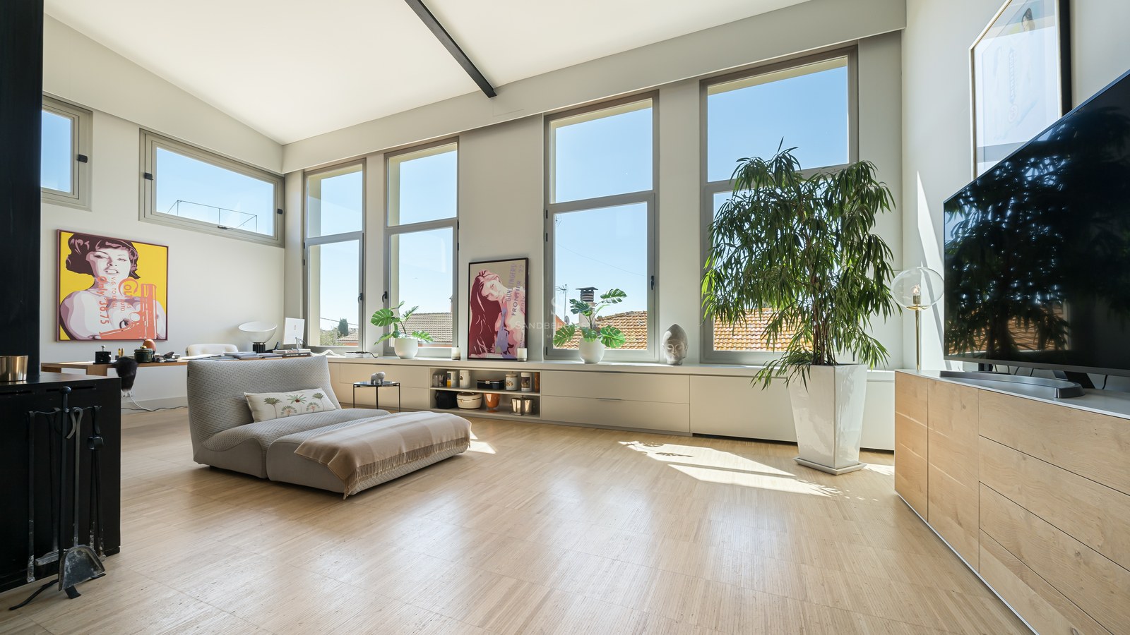 Heller Wohnraum mit Eichenparkett, großen vertikalen Fenstern, niedriger Liege und Pop-Art an weißen Wänden.