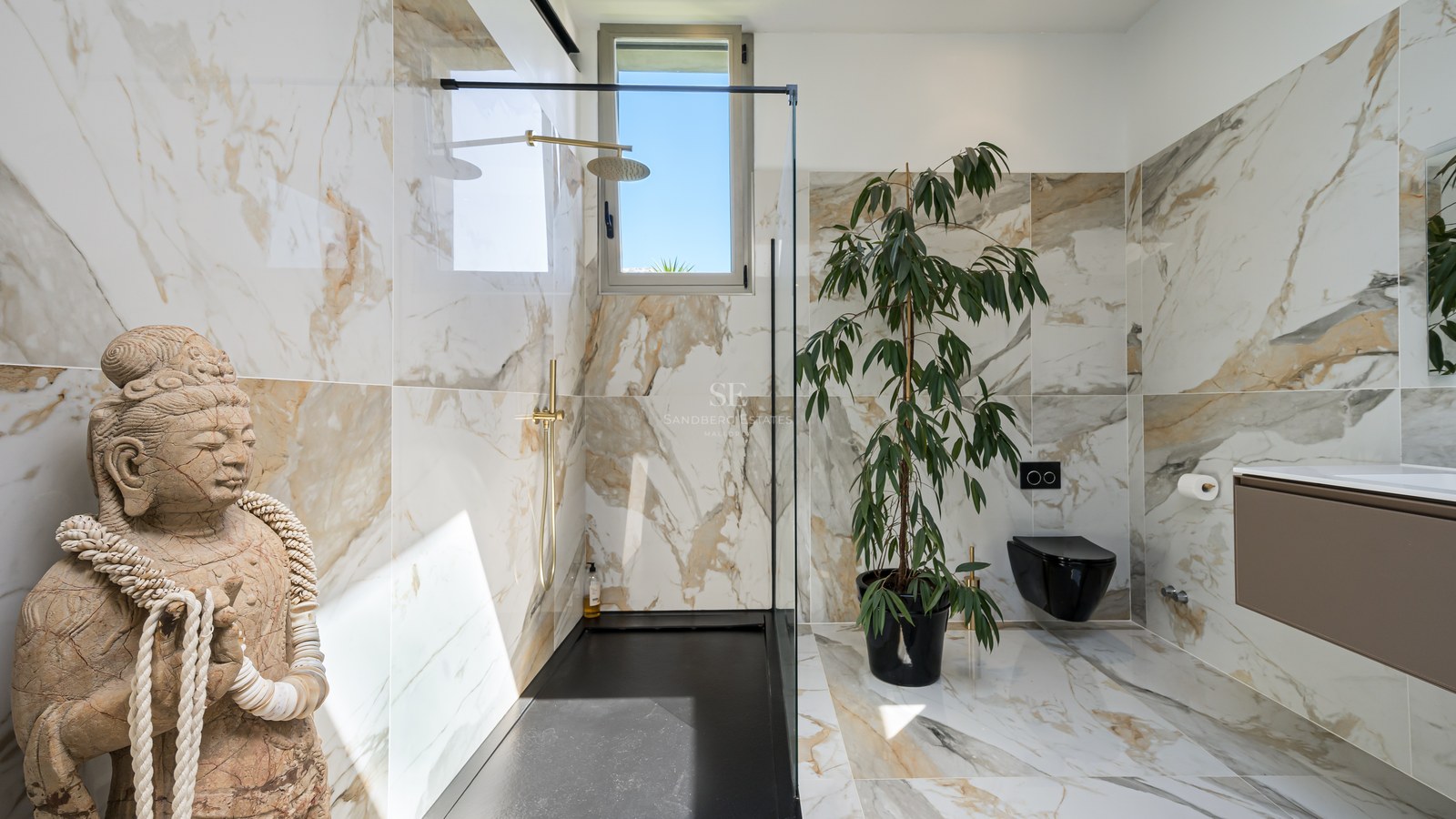 Modernes Badezimmer mit Marmorfliesen, schwarzer begehbarer Dusche, goldenen Armaturen und einer Buddha-Steinfigur.