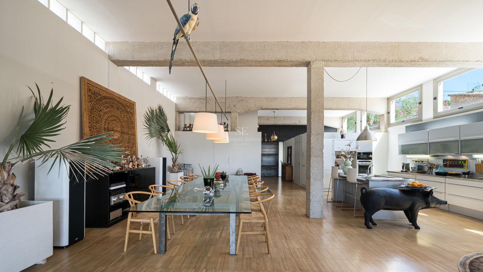 Offener Essbereich mit Sichtbetonbalken, großem Glastisch und moderner Küche in lichtdurchflutetem Loft.