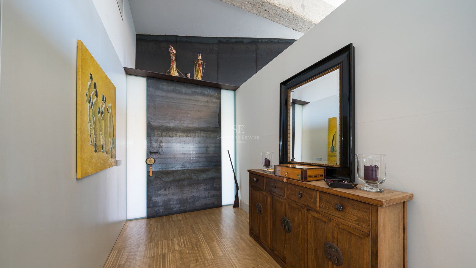 Flur mit großer industrieller Stahltür, Sideboard aus Holz mit Spiegel und zeitgenössischer Kunst.
