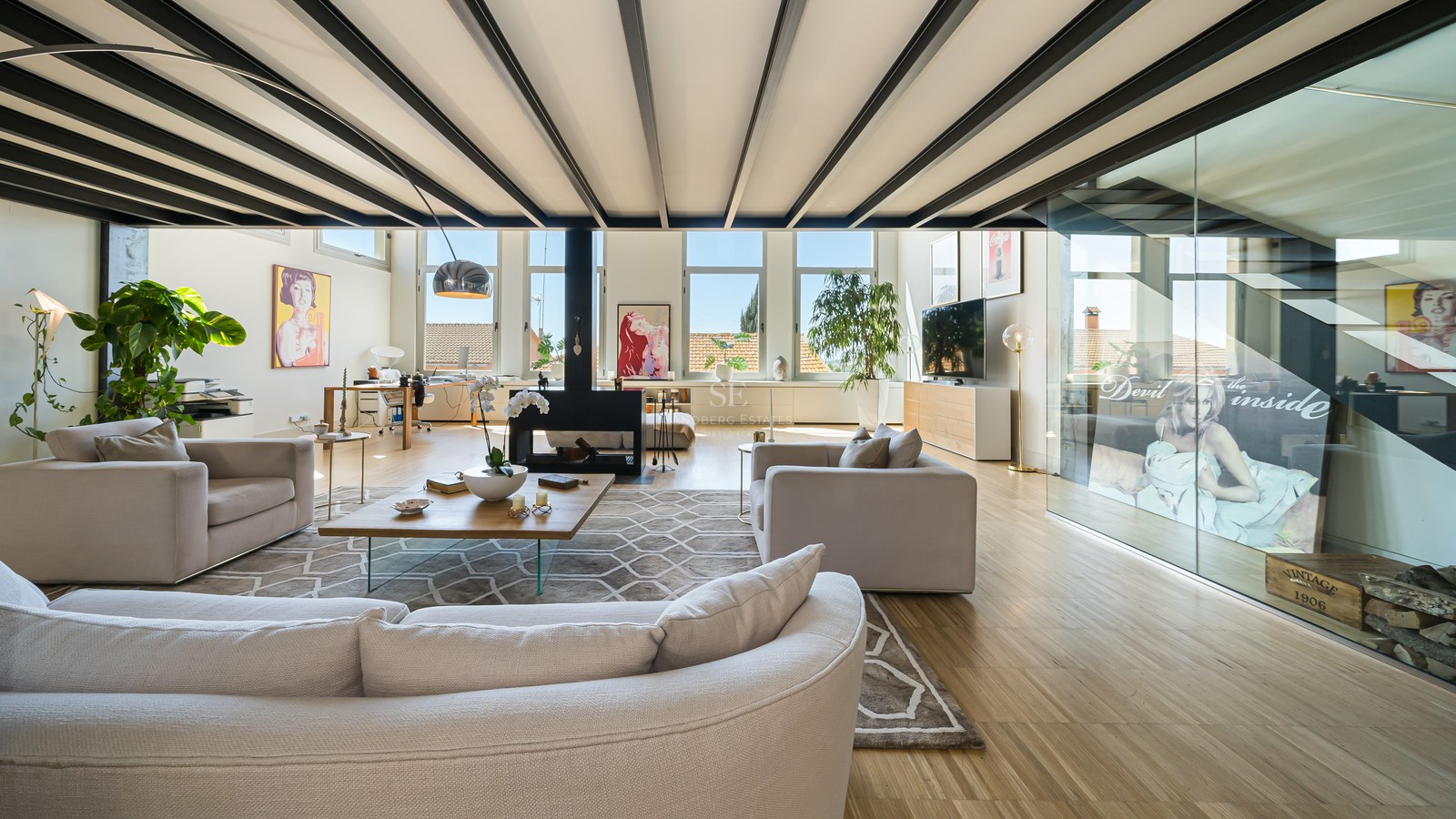 Helles Wohnzimmer mit schwarzen Stahlbalken, cremefarbenen Sofas, zentralem Kamin und großen Fenstern.