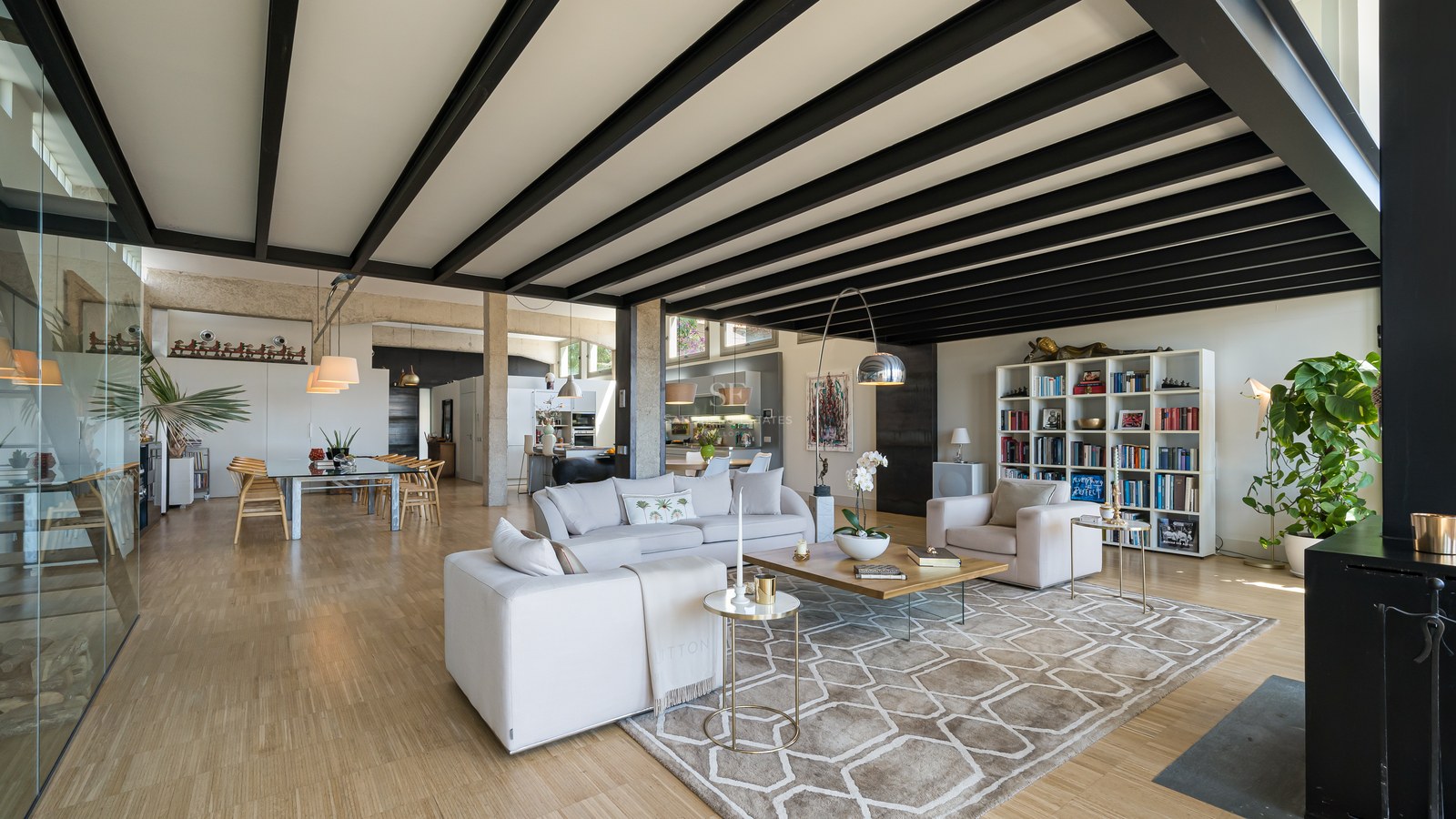 Großzügiges Wohnzimmer mit schwarzen Stahlbalken, hellem Holzfußboden und weißen Sofas in einer offenen Luxusvilla.