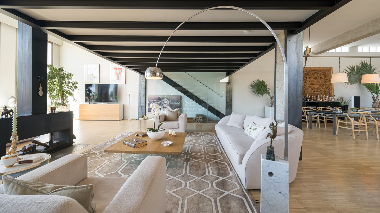 Großzügiges modernes Wohnzimmer mit schwarzen Stahlbalken, cremefarbenem Sofa und gläsernem Treppenhaus.