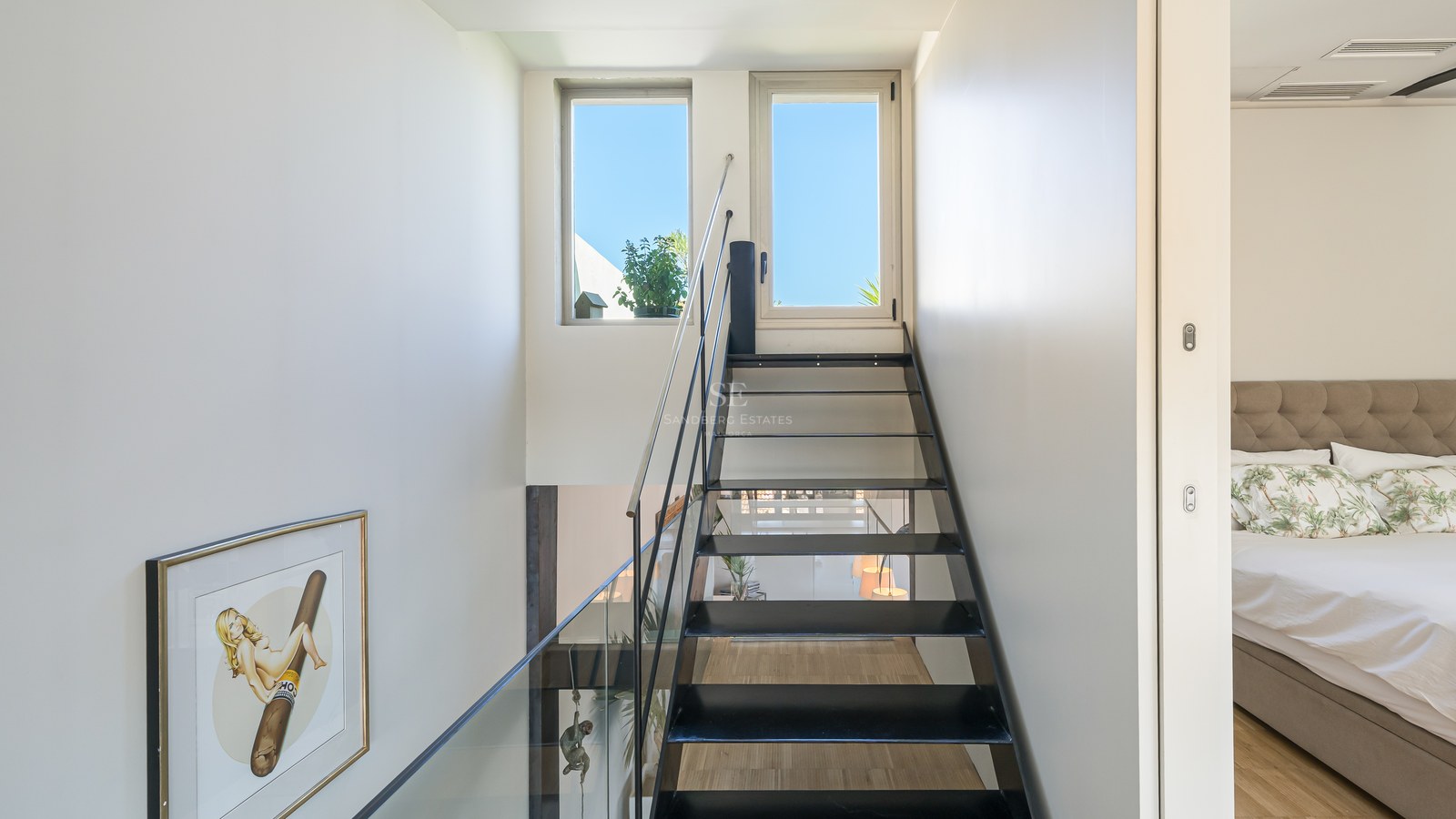 Schwarze Stahltreppe mit Glasgeländer und Blick auf den blauen Himmel durch die oberen Fenster.